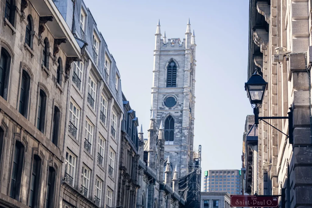 Old Montreal street framed by stone buildings with a church tower in the distance.