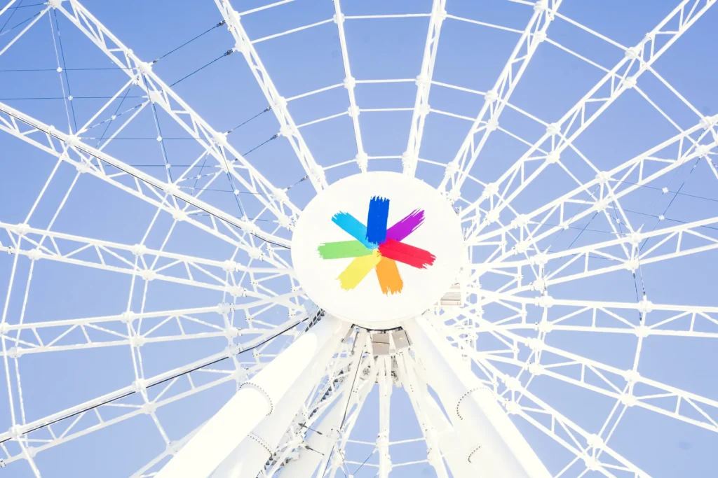 Colourful centre and white spokes of La Grande Roue de Montréal against a blue sky.