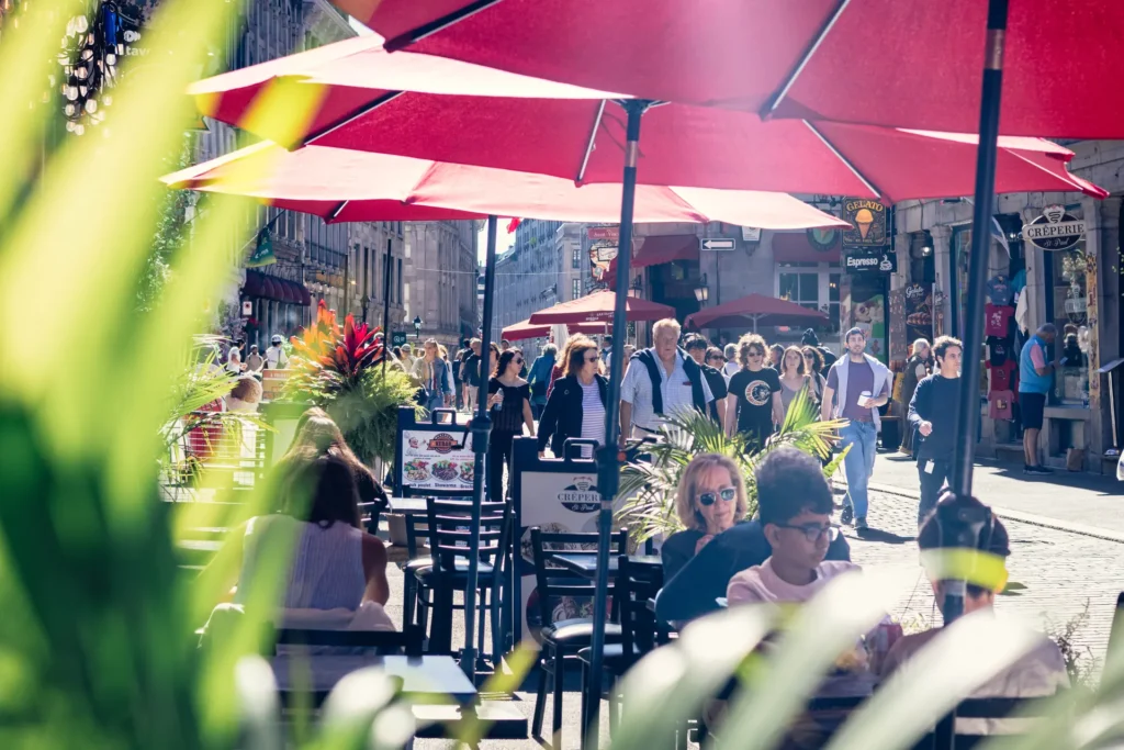 Busy outdoor terrace with red umbrellas and greenery in Old Montreal.